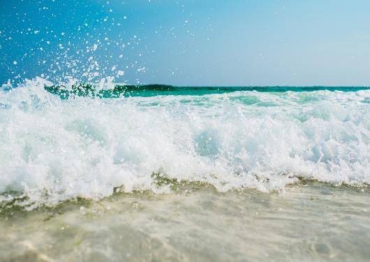 Wellen brechen am Strand unter klarem Himmel.