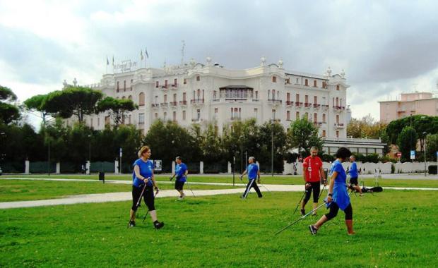 Persone praticano nordic walking in un parco verde vicino a un edificio storico.