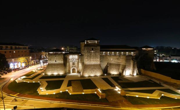 Castello illuminato di notte, circondato da strade e giardini.