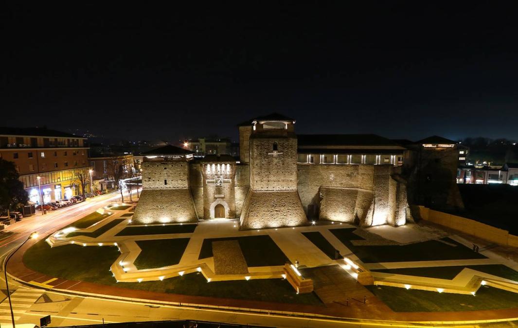 Castello illuminato di notte, circondato da strade e giardini.